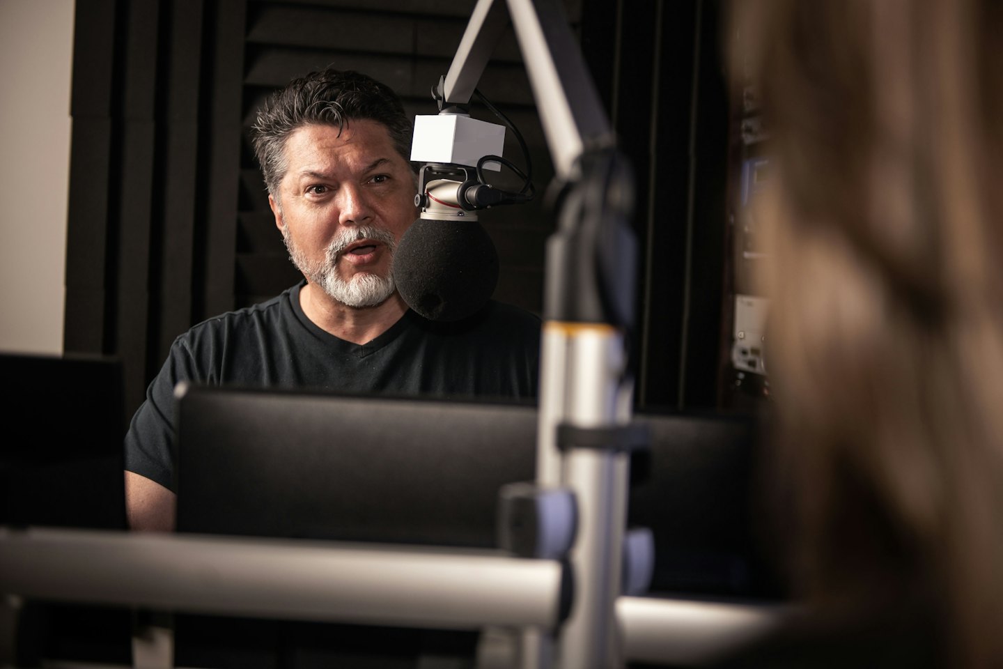 Mężczyzna z siwą brodą mówi do mikrofonu podcastowego.